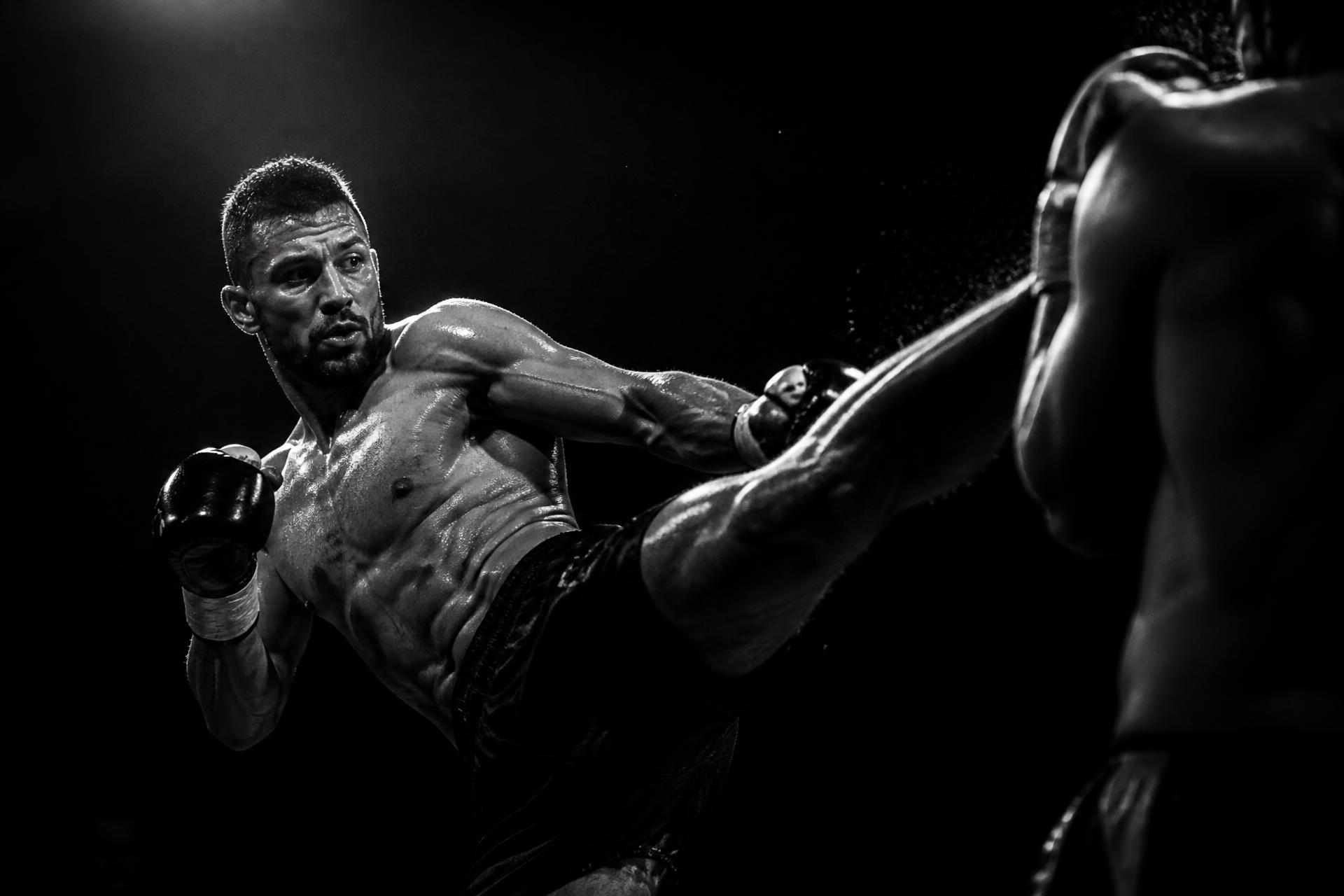 Kickboxer delivering a high kick in a dark arena